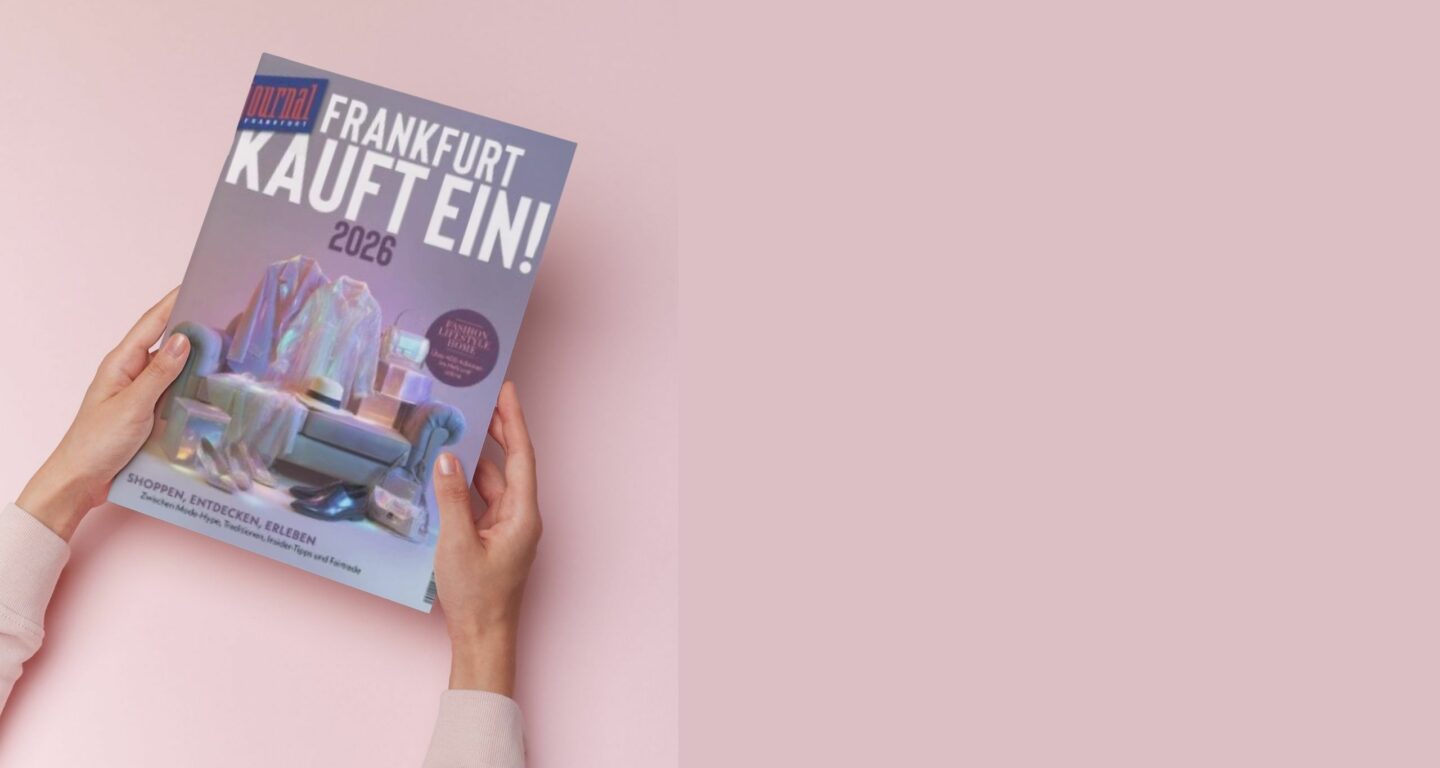 Zwei Hände halten eine Zeitschrift mit dem Titel Frankfurt Kauft Ein! 2026 vor einem rosa Hintergrund. Das holografische Cover mit einer Einkaufstasche und einem Stuhl weist auf die neuesten Trends des Möbelhauses Bad Homburg hin.