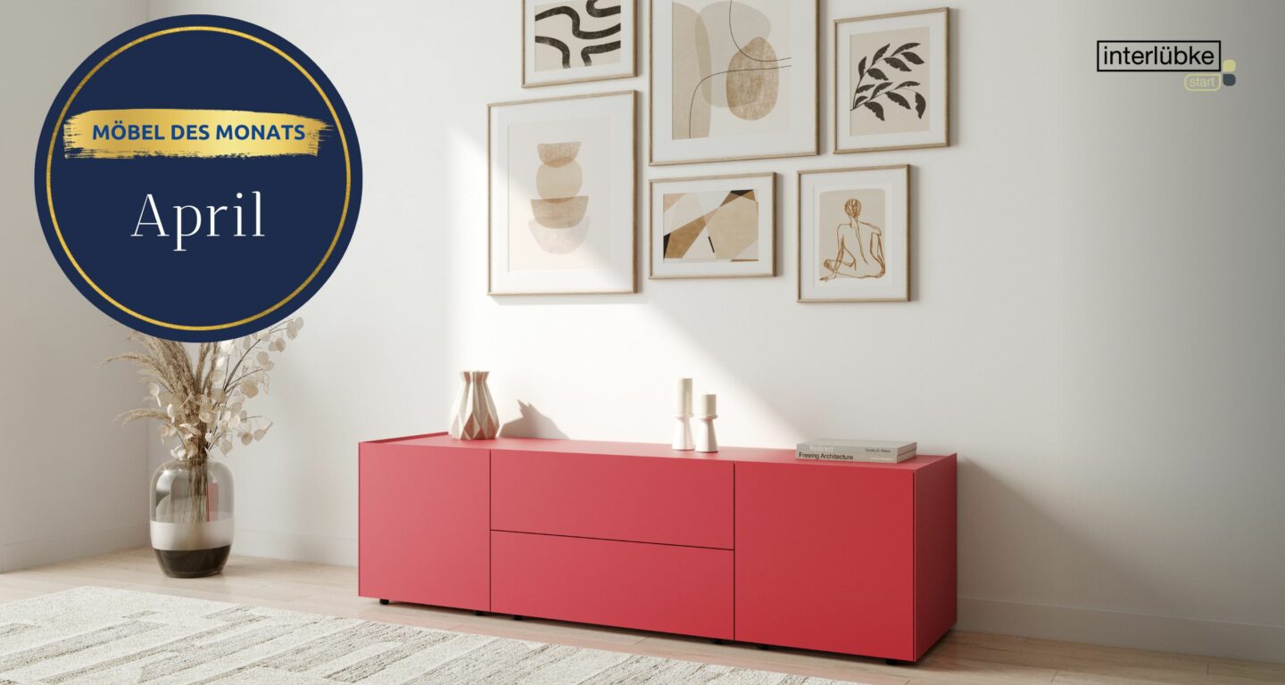 Ein modernes Wohnzimmer mit einem roten Sideboard, minimalistischen Kunstwerken an einer weißen Wand und einem runden Schild mit der Aufschrift Möbel des Monats April, das den zeitgenössischen Geschmack des Möbelhauses Bad Homburg widerspiegelt.