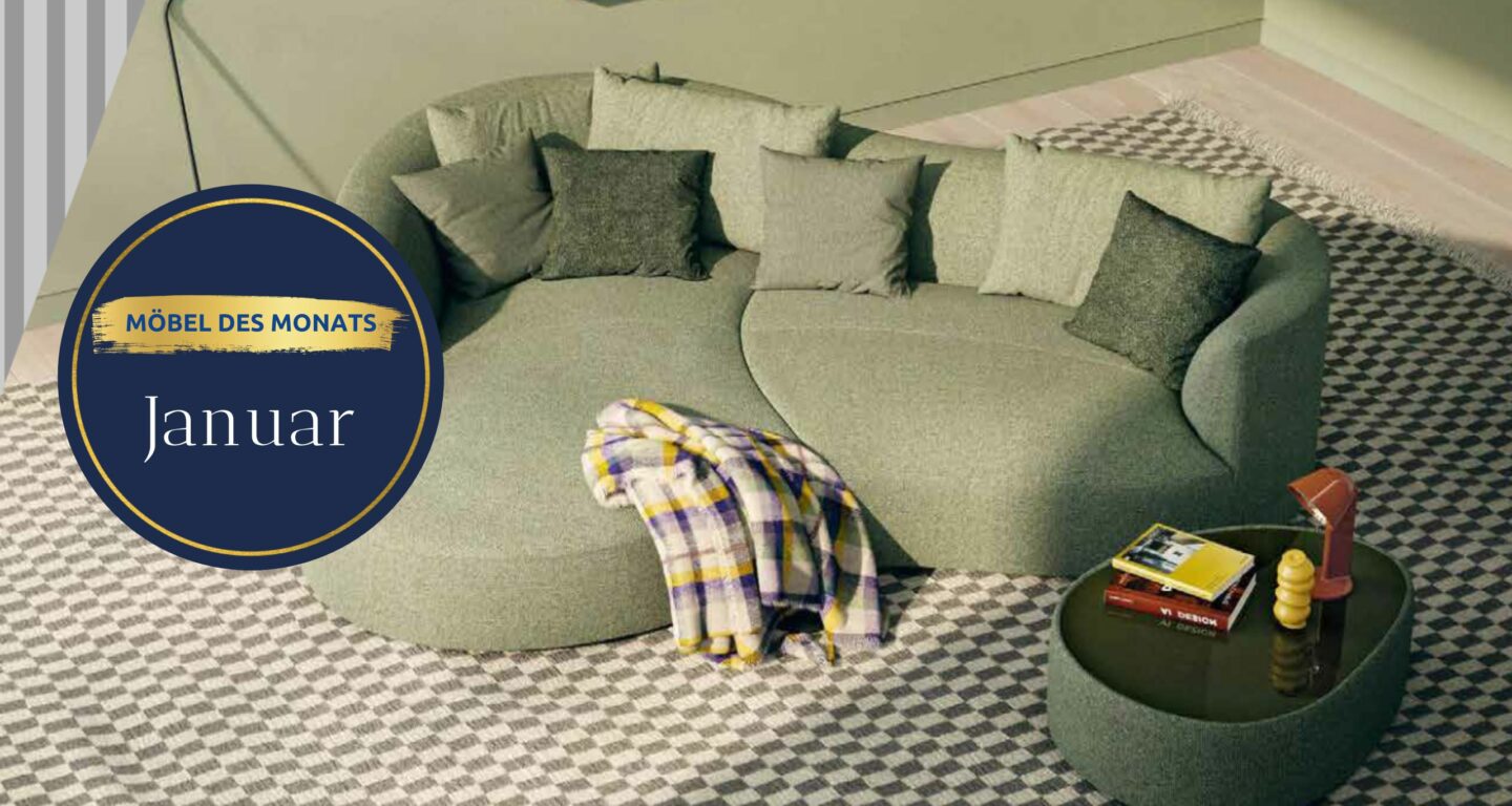 Ein geschwungenes grünes Sofa mit verschiedenen grauen Kissen und einer karierten Decke, daneben ein runder schwarzer Couchtisch mit Büchern und einer Lampe, auf einem gemusterten Teppich - entdecken Sie diesen Look im Möbelhaus Bad Homburg.