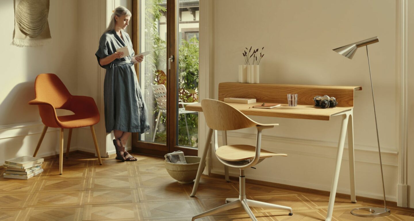 Eine Frau steht an einer Glastür und liest in einem hellen Raum mit Holzschreibtisch, modernem Stuhl und Dekoration - ein eleganter Raum, der vom Möbelhaus Bad Homburg inspiriert ist.