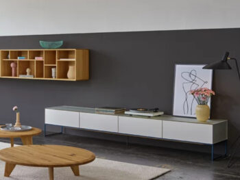 Modernes Wohnzimmer mit einer niedrigen weißen cubus pure Medienkonsole von Team 7, einem Couchtisch aus Holz, Wandregalen, Kunstwerken und einer Stehlampe vor einer zweifarbigen Wand für einen stilvollen Wohnwand-Look.