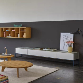 Modernes Wohnzimmer mit einer niedrigen weißen cubus pure Medienkonsole von Team 7, einem Couchtisch aus Holz, Wandregalen, Kunstwerken und einer Stehlampe vor einer zweifarbigen Wand für einen stilvollen Wohnwand-Look.