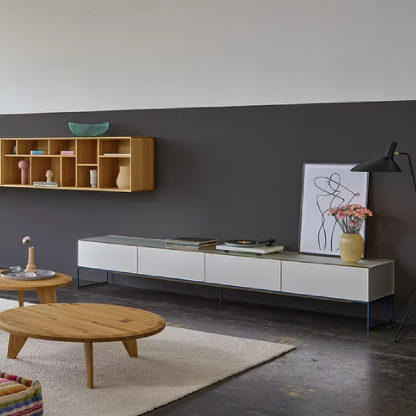 Modernes Wohnzimmer mit einer niedrigen weißen cubus pure Medienkonsole von Team 7, einem Couchtisch aus Holz, Wandregalen, Kunstwerken und einer Stehlampe vor einer zweifarbigen Wand für einen stilvollen Wohnwand-Look. Modernes Wohnzimmer mit einer niedrigen weißen cubus pure Medienkonsole von Team 7, einem Couchtisch aus Holz, Wandregalen, Kunstwerken und einer Stehlampe vor einer zweifarbigen Wand für einen stilvollen Wohnwand-Look.