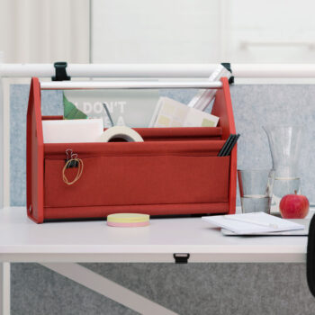 Ein roter Vitra Locker Box Schreibtisch-Organizer mit Ordnern, Notizbüchern, Stiften und Büromaterialien steht auf einem weißen Schreibtisch mit einem Glas Wasser, einem Apfel, einem Notizblock und Papieren.
