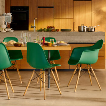 Moderne Küche und Essbereich mit Holztisch, grünen Stühlen, Geschirr und Gläsern für eine Mahlzeit; Holzschränke und Arbeitsplatte im Hintergrund.