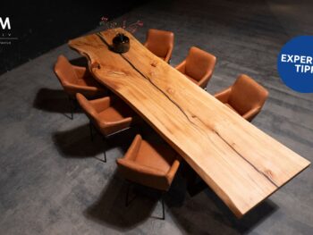 Großer Form Exclusiv Esstisch Monolith mit natürlicher Maserung, umgeben von acht braunen Lederstühlen auf einem Betonboden; eine schwarze Vase mit Zweigen steht auf dem Tisch, entworfen von Marcus Braum.