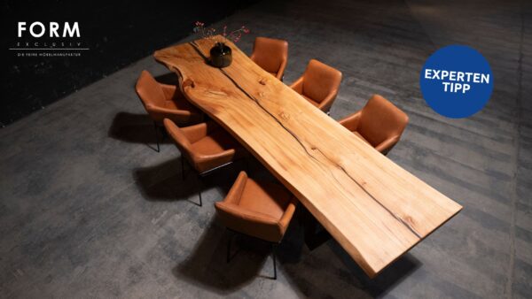 Großer Form Exclusiv Esstisch Monolith mit natürlicher Maserung, umgeben von acht braunen Lederstühlen auf einem Betonboden; eine schwarze Vase mit Zweigen steht auf dem Tisch, entworfen von Marcus Braum.