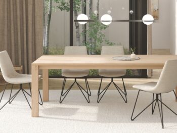 Modernes Esszimmer mit einem TEAM 7 Light Holztisch, vier beigefarbenen Stühlen mit schwarzen Metallbeinen, einem runden Tablett und großen Fenstern, die den Blick auf die Bäume im Freien freigeben - Teil der Kollektion Schnellliefersortiment Essentials.