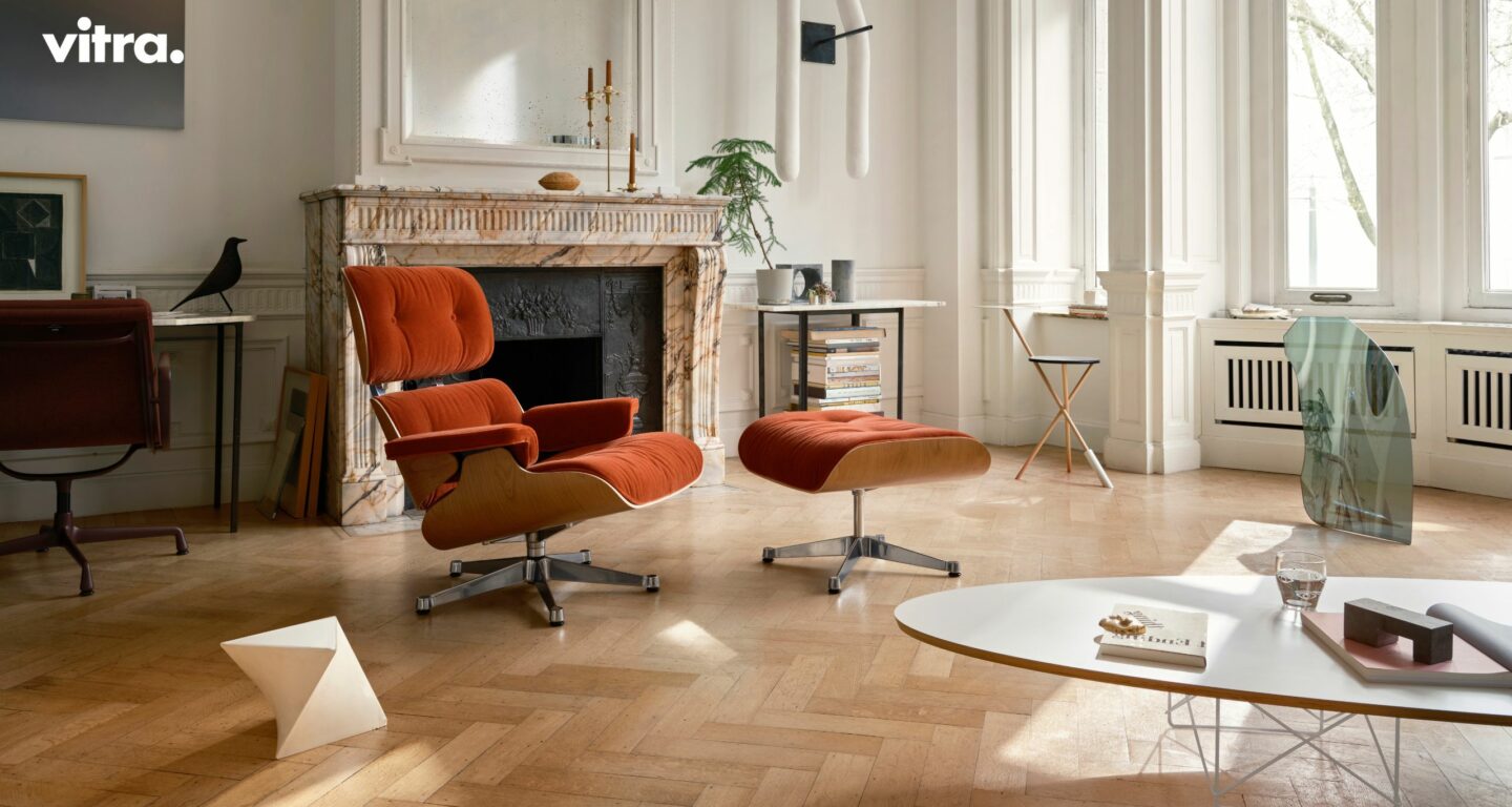 Ein Wohnzimmer mit einem orangefarbenen Sessel und einer Ottomane vom Möbelhaus Bad Homburg, einem Marmorkamin, einem kleinen Schreibtisch und großen Fenstern, die viel Tageslicht hereinlassen. Ein Wohnzimmer mit einem orangefarbenen Sessel und einer Ottomane vom Möbelhaus Bad Homburg, einem Marmorkamin, einem kleinen Schreibtisch und großen Fenstern, die viel Tageslicht hereinlassen.