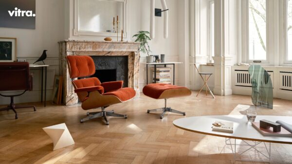 Ein modernes Wohnzimmer mit einem Marmorkamin, einem orangefarbenen Loungesessel und einer Ottomane, einem Schreibtisch, großen Fenstern und minimalistischem Dekor schafft einen gemütlichen Rückzugsort im Winter, inspiriert von Vitra Homestories und einem Gefühl von Harmonie.