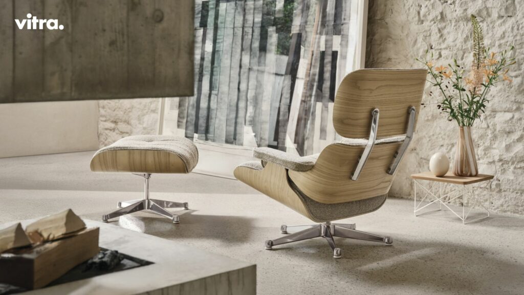 Ein moderner Loungesessel mit passender Ottomane mit Holz- und Metallakzenten steht auf einem hellen Steinboden neben einem kleinen Beistelltisch mit einer Blumenvase und schafft in diesem minimalistischen Raum Winterharmonie zu Hause - perfekt zum Entspannen.