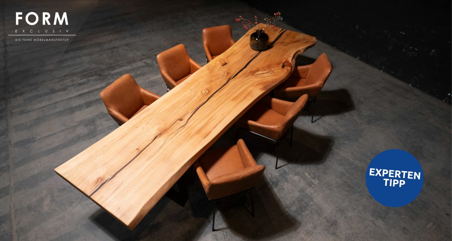 Ein großer Esstisch aus Holz mit Naturkante, erhältlich im Möbelhaus Bad Homburg, wird von acht braunen Lederstühlen auf einem dunklen Boden umgeben. Eine schwarze Vase mit Zweigen steht elegant auf dem Tisch.