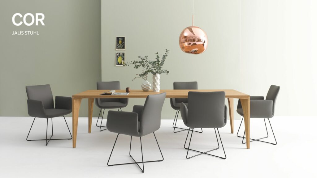 Modernes Esszimmer mit einem COR Jalis Stuhl um einen Holztisch, sechs grauen Stühlen mit Metallbeinen, einer kupfernen Pendelleuchte, einer Vase mit Grünzeug und zwei kleinen Wandbildern - perfekt für jede Gelegenheit oder Aktion.